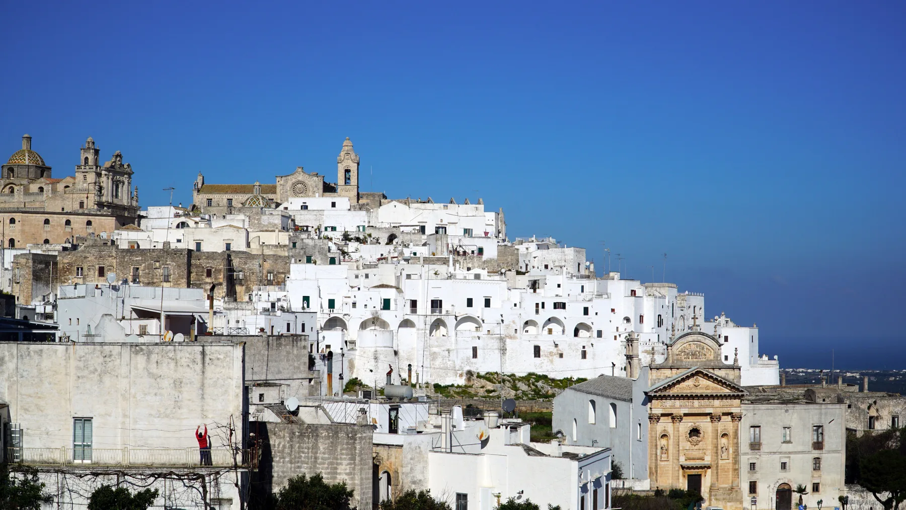 Un pueblo en la ladera, con edificios blancos e iglesias históricas de piedra bajo un cielo azul despejado.