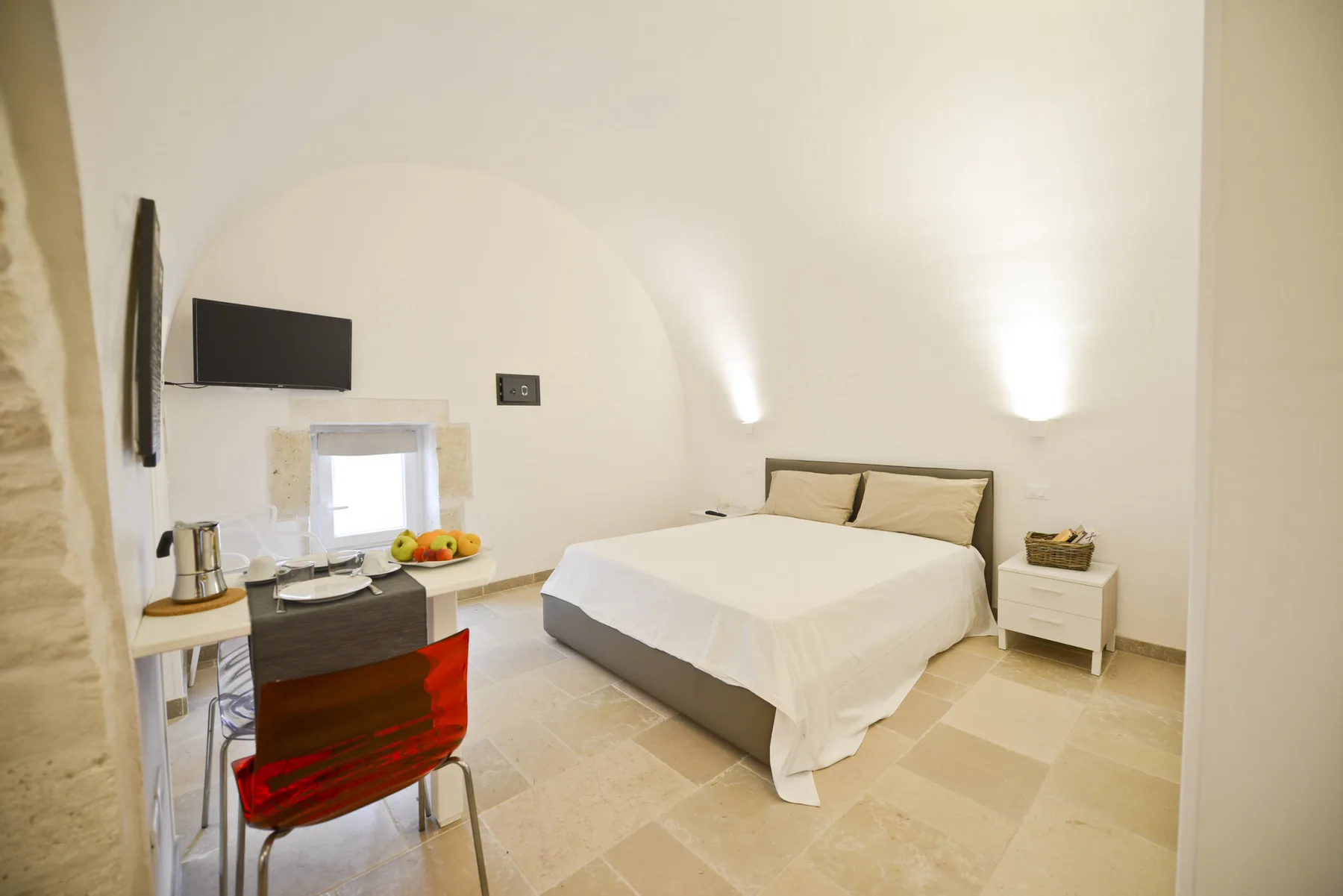 A bright bedroom with a bed, bedside table, and small desk.