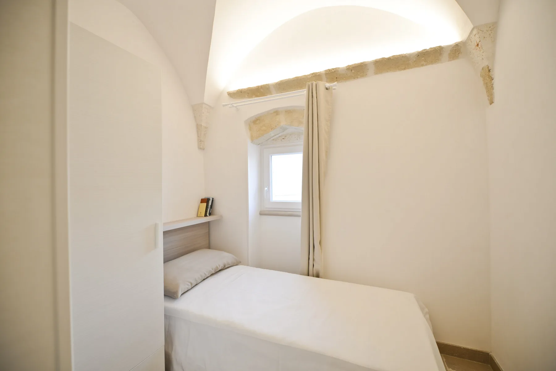 Un dormitorio pequeño con una cama bajo una ventana estrecha.