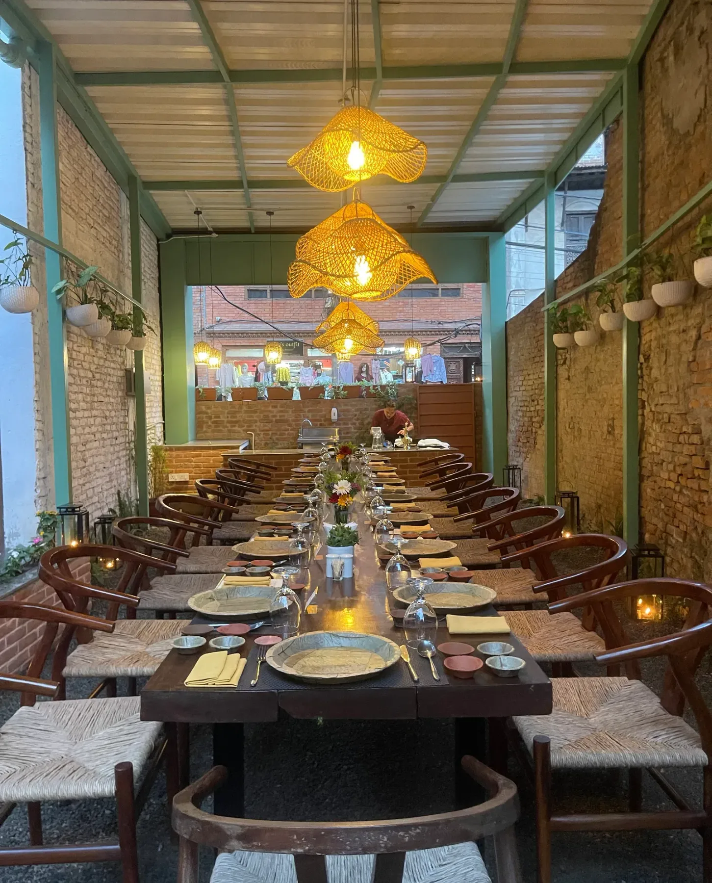 Dining table beneath woven pendant lights in a semi-outdoor corridor.