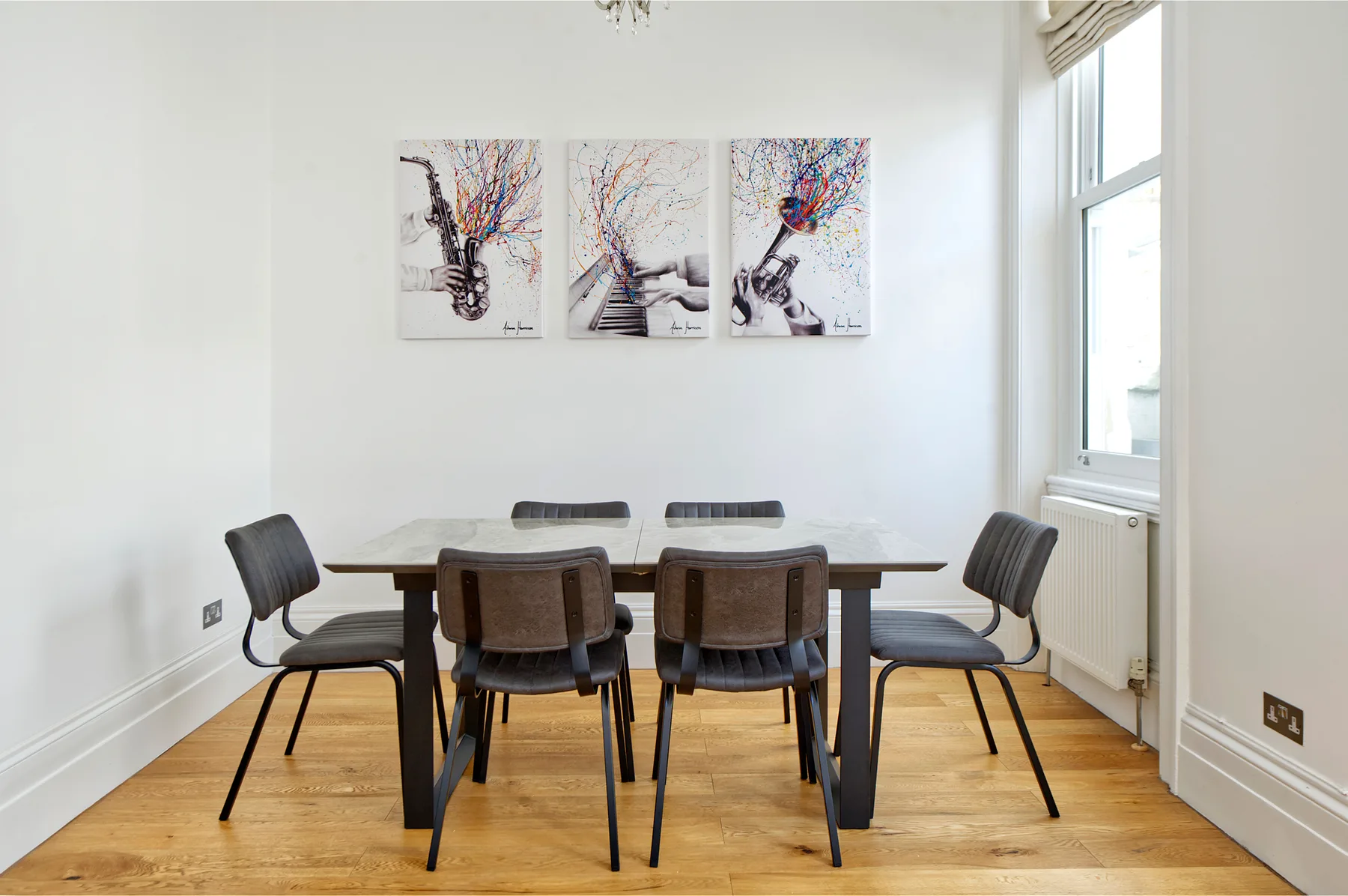 A dining area with a rectangular table and chairs beneath three wall prints.