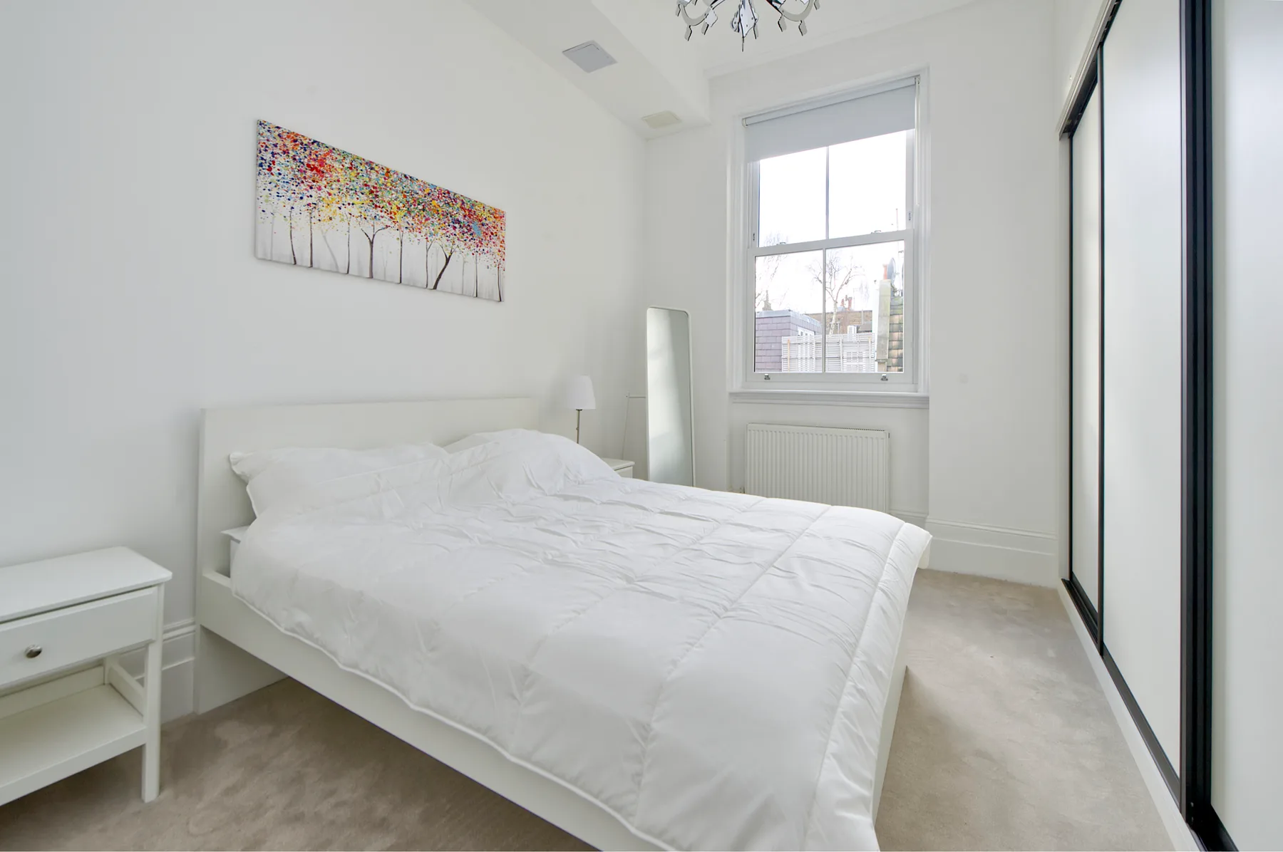 A bright bedroom with a white bed and a large window.