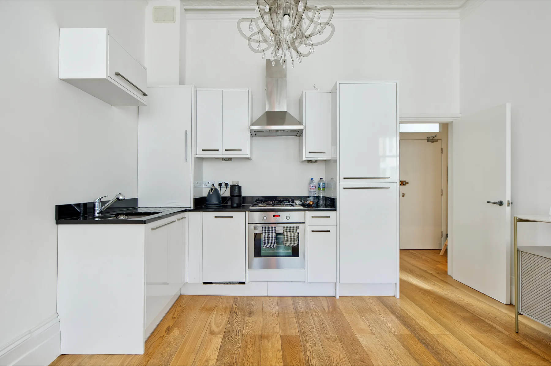 A bright white kitchen with cabinets, a stove, and wooden flooring.