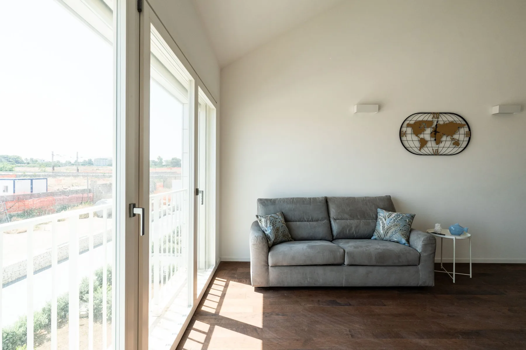 Una sala luminosa con un sofá gris junto a grandes ventanas.