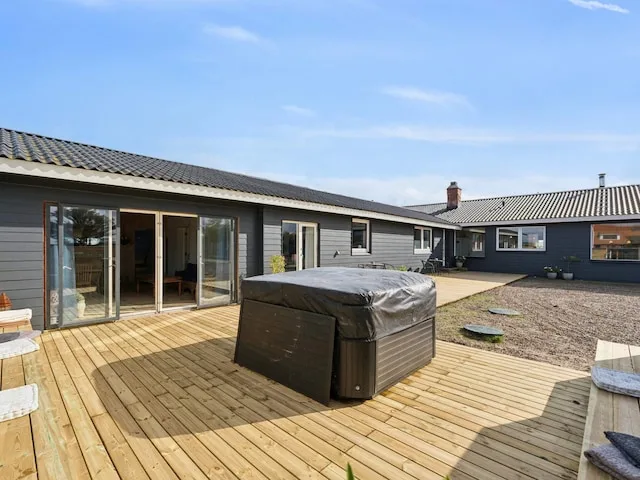 A single-story house opens onto a wooden deck with a covered hot tub.
