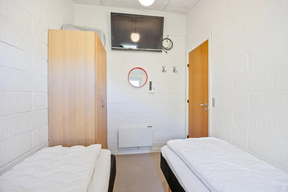 Un dormitorio luminoso con dos camas individuales y un televisor en la pared.