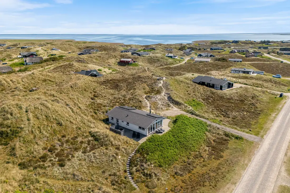 Vista aérea de un paisaje de dunas costeras con casas dispersas y una carretera.