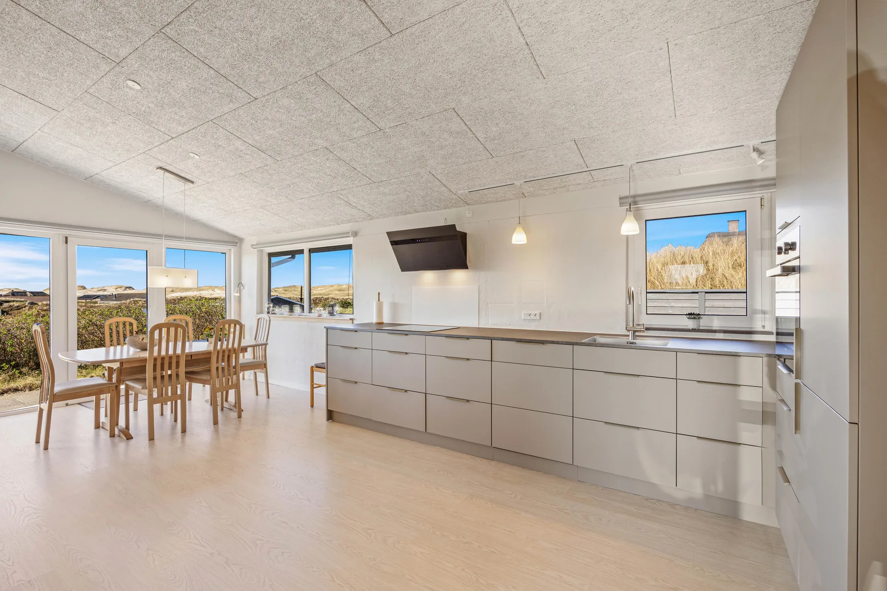Una cocina luminosa con una encimera larga y una mesa junto a las ventanas.
