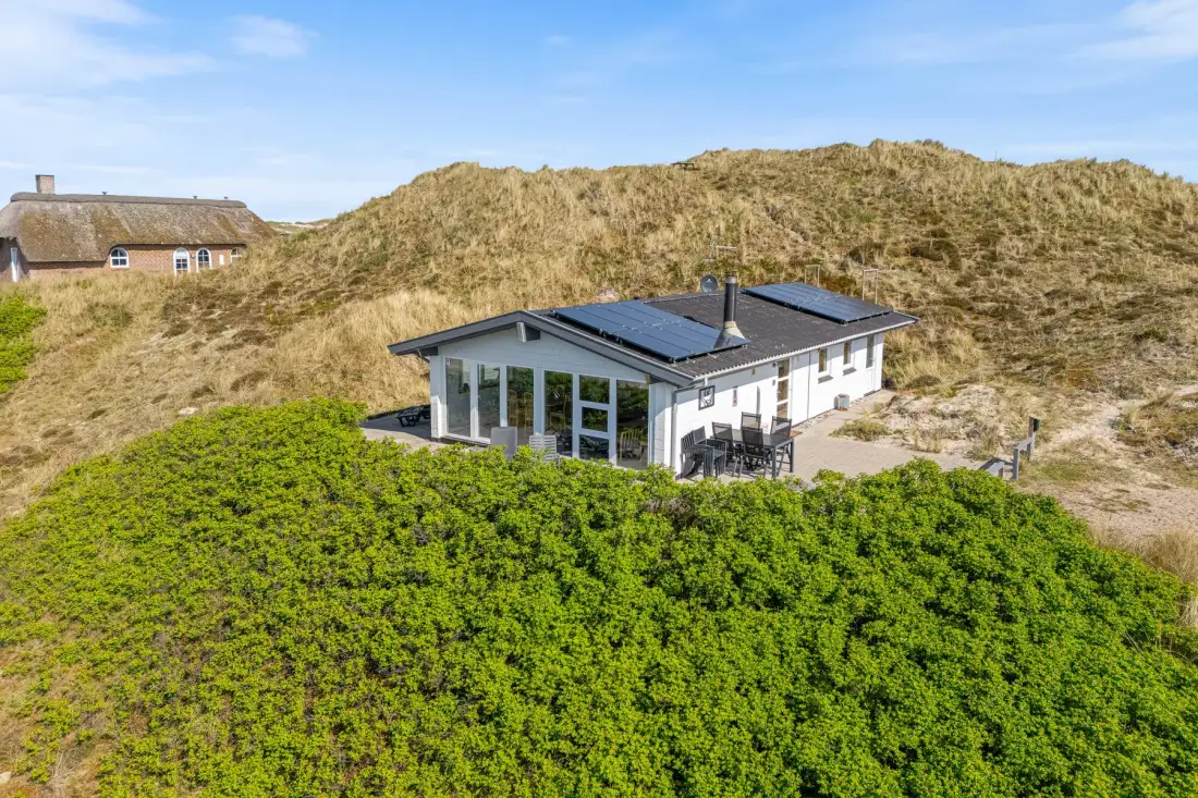 Una casa moderna está entre arbustos verdes junto a una duna de arena.
