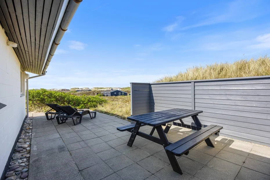 Un patio al aire libre con mesas de picnic y asientos reclinables junto a una cerca gris.
