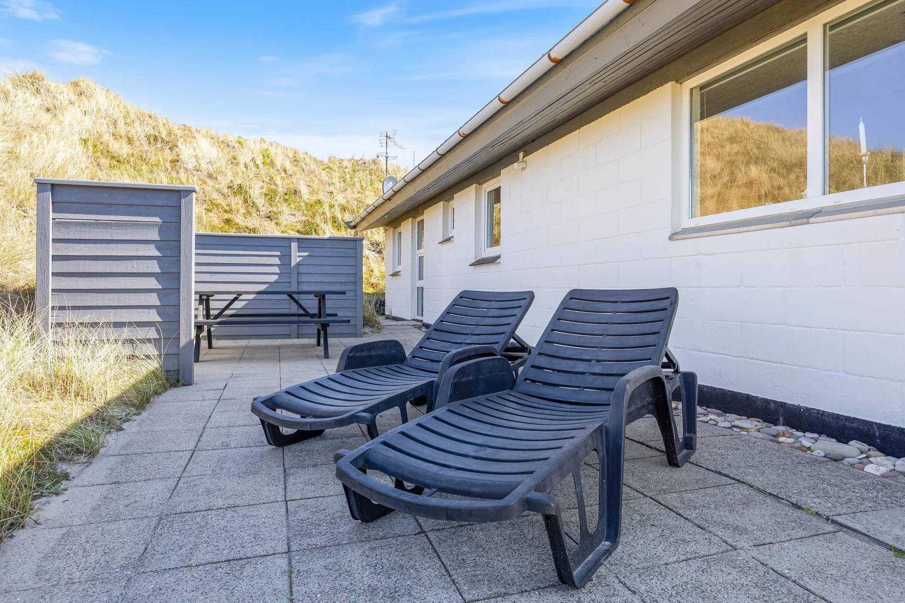 Un patio exterior con tumbonas reclinables junto a una casa blanca.