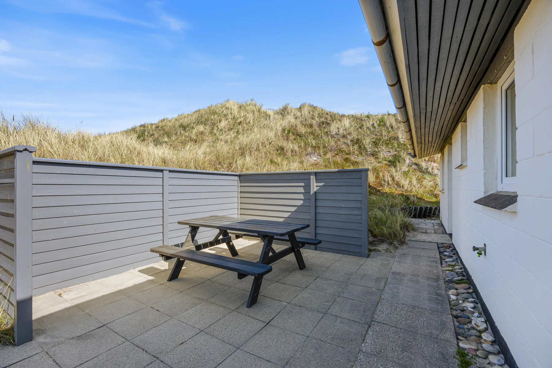 Un patio exterior pavimentado con una mesa de picnic junto a una casa y rodeado por paneles grises.