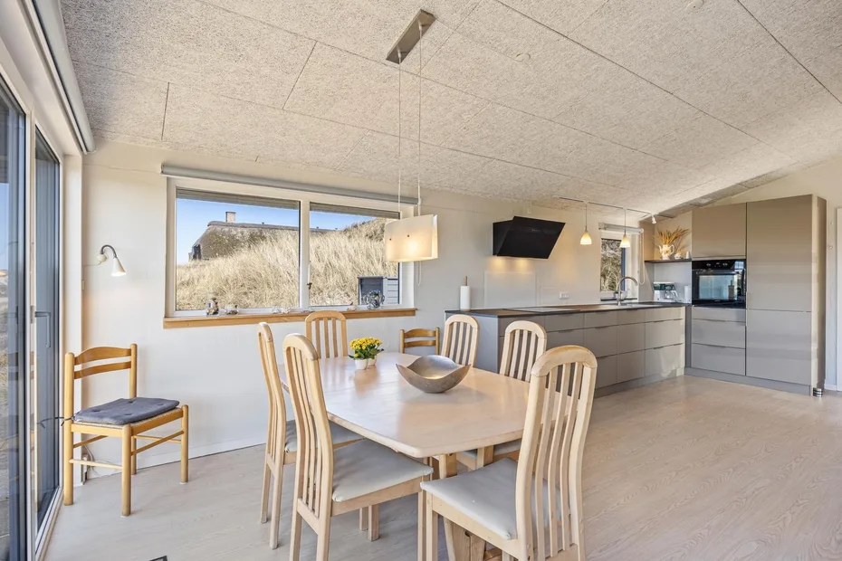 Comedor y cocina de concepto abierto, con una mesa de madera junto a grandes ventanas.
