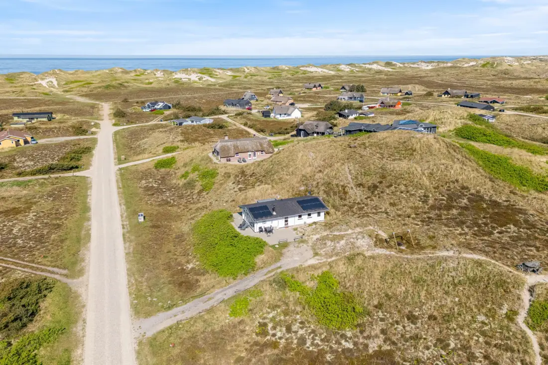Vista aérea de casas dispersas entre dunas arenosas, con el mar en el horizonte.