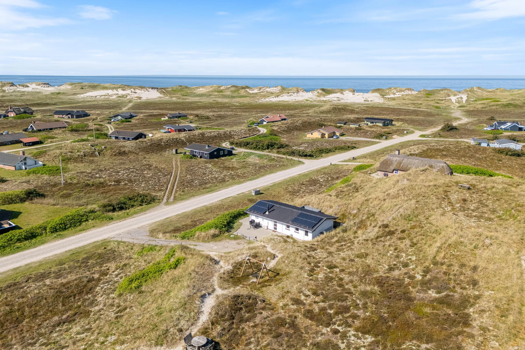 Vista aérea de casas dispersas junto a un camino entre dunas costeras.