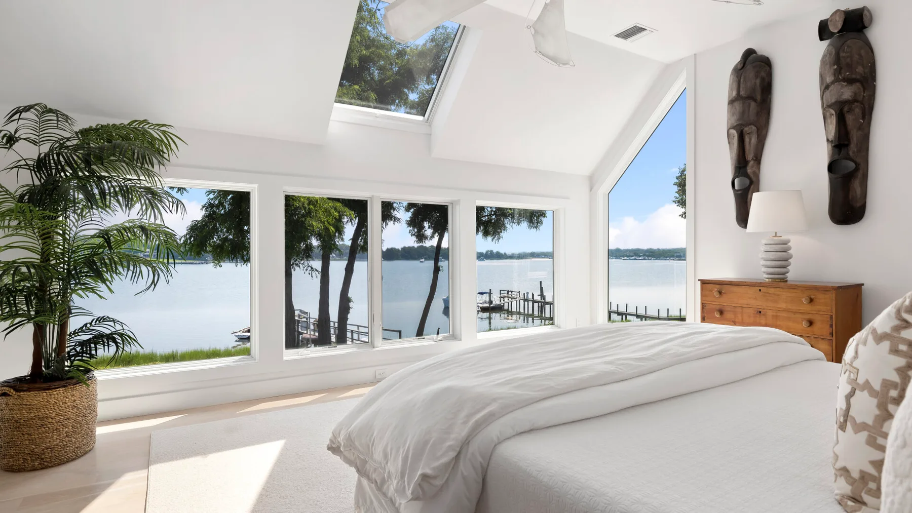 A bright bedroom with a large bed, windows, and a view of the water.