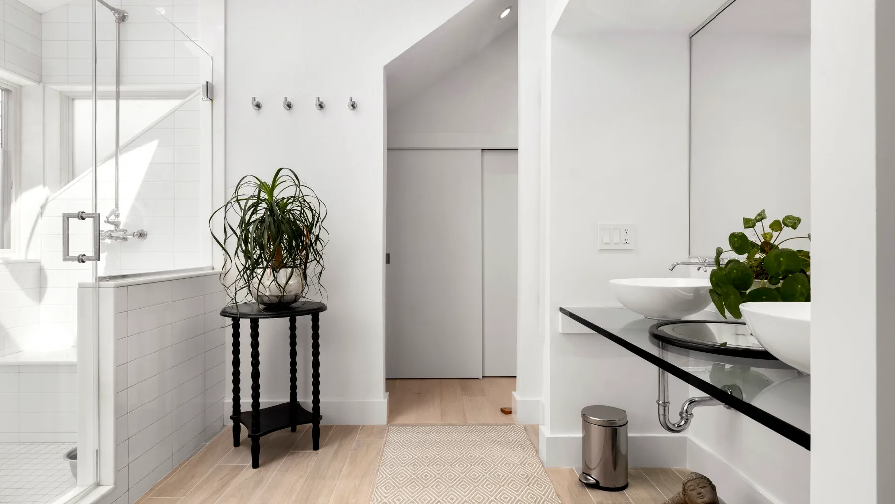 A bright bathroom with a glass shower and a plant beside the vanity.