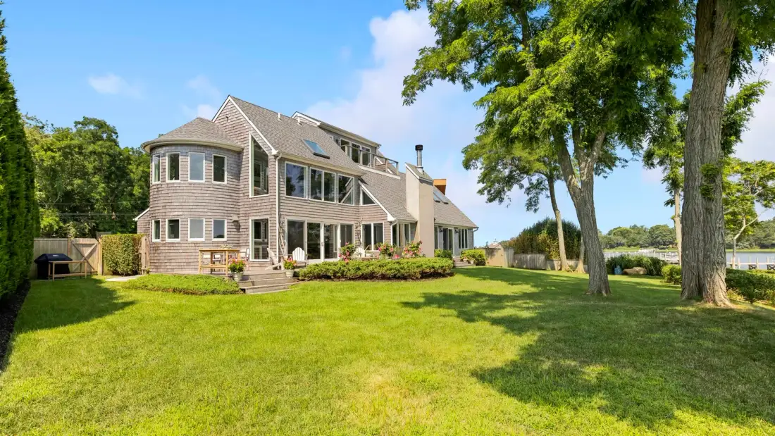 A large house stands beyond a broad green lawn, with mature trees nearby.