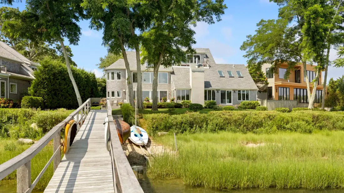 A wooden boardwalk crosses grassy wetlands toward a large building.