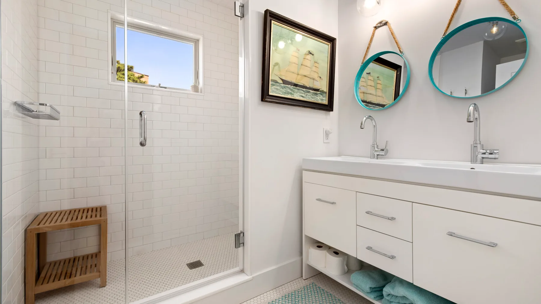 A bright bathroom with a glass shower and a double-sink vanity.