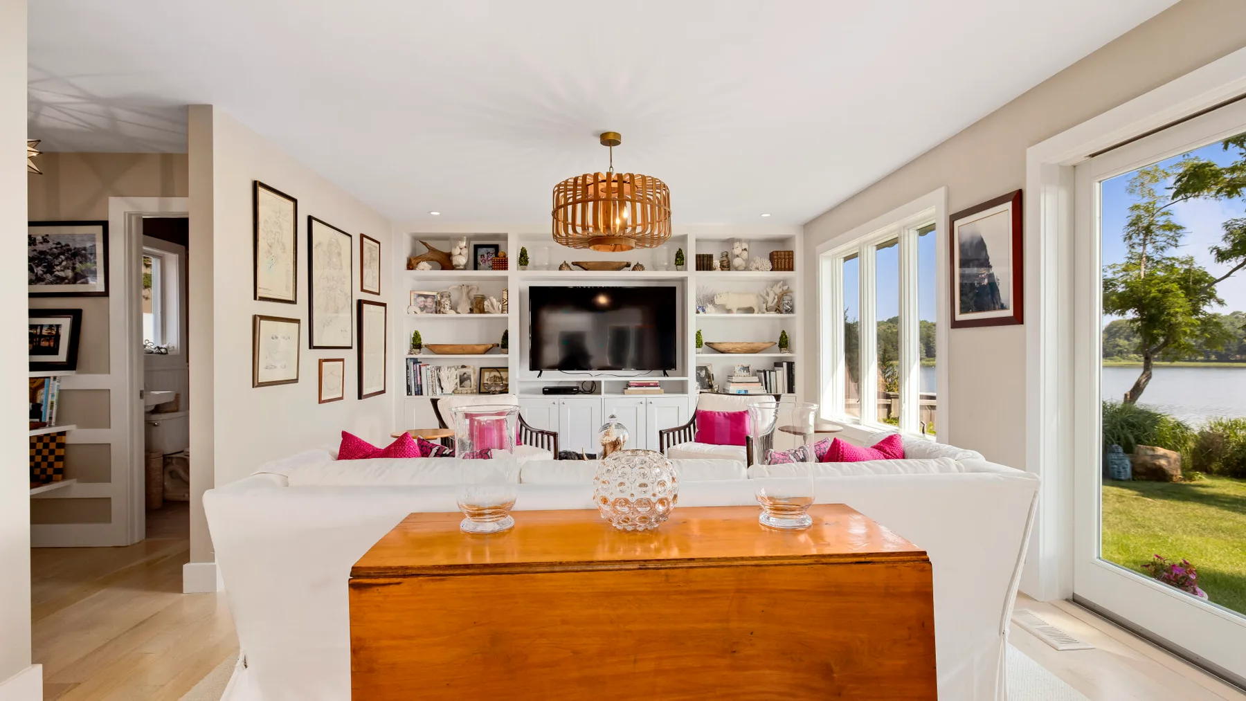 A bright living room with white seating, built-in shelves, and a large television.
