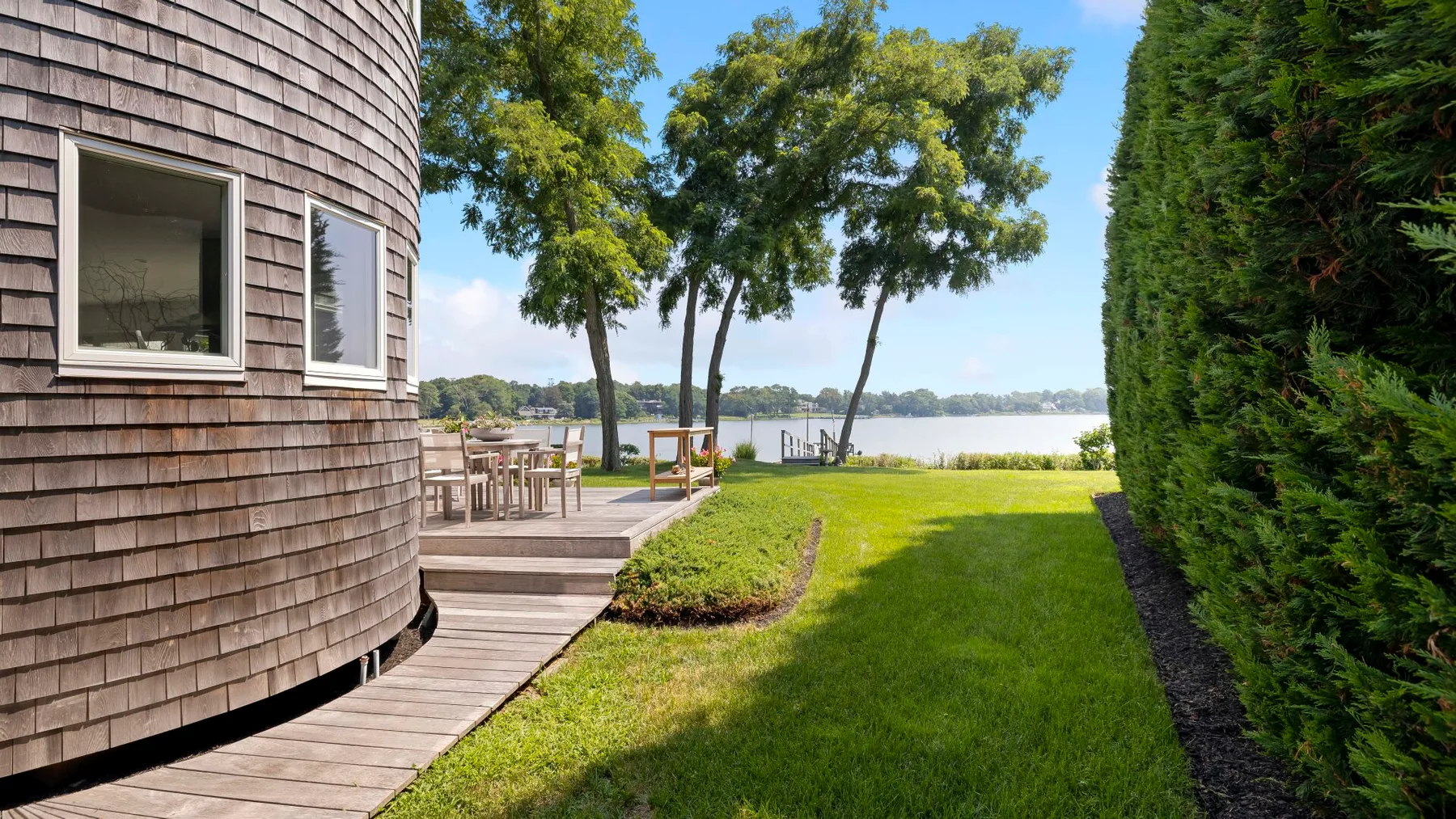 A lakeside lawn beside a curved shingled building and wooden deck.