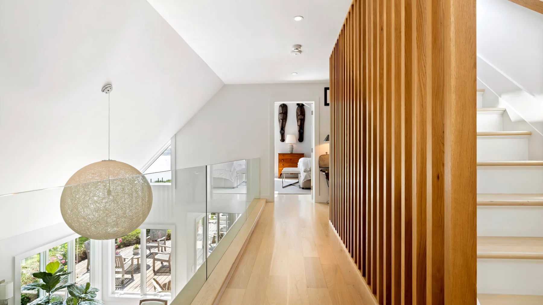 A bright upper-level hallway with a glass railing and wood slat partition.