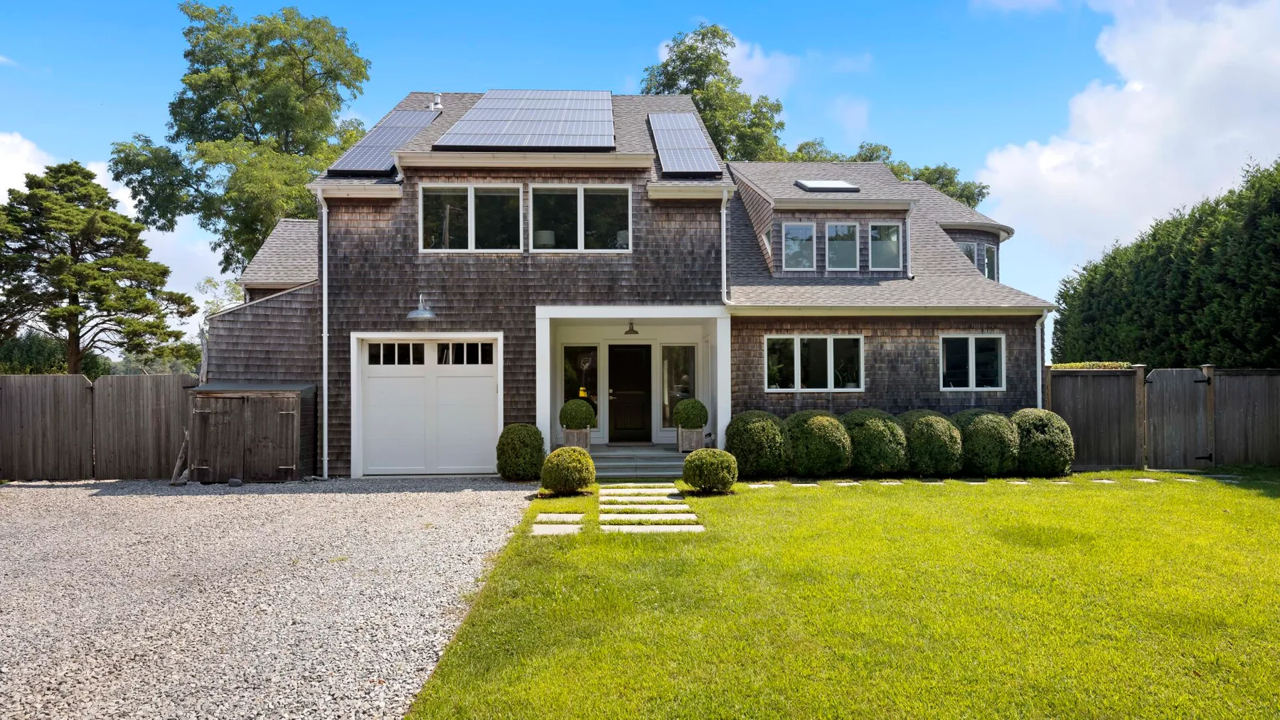 A large house with solar panels faces a lawn and gravel driveway.