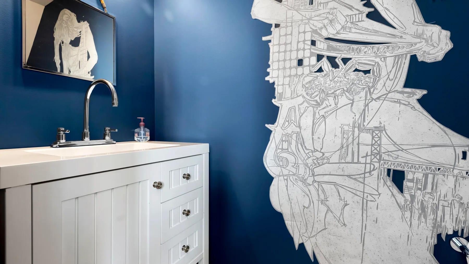 A bathroom vanity with a sink stands against a blue wall beside a large white line drawing.