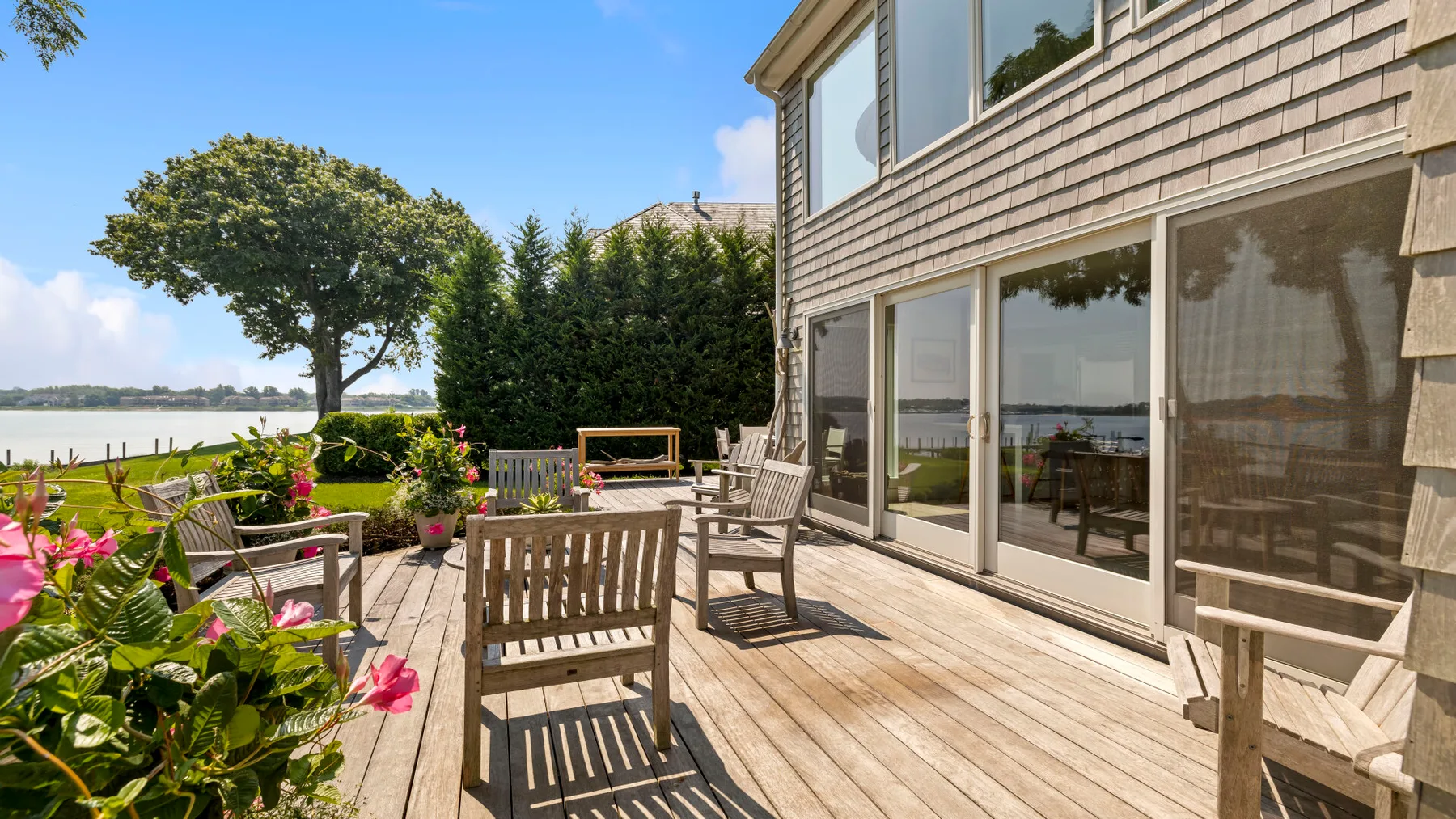 A wooden deck beside a house overlooks a landscaped garden and water.