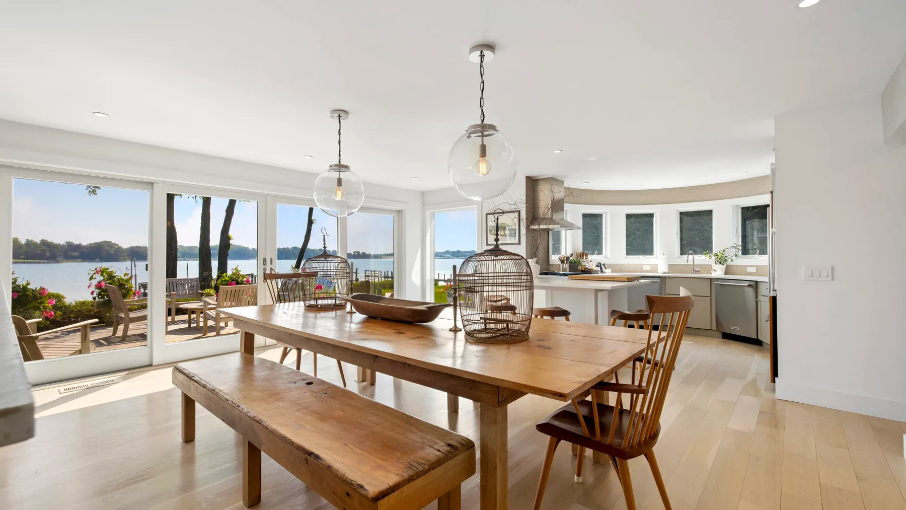 A bright dining area opens onto a kitchen, with large windows overlooking the water.