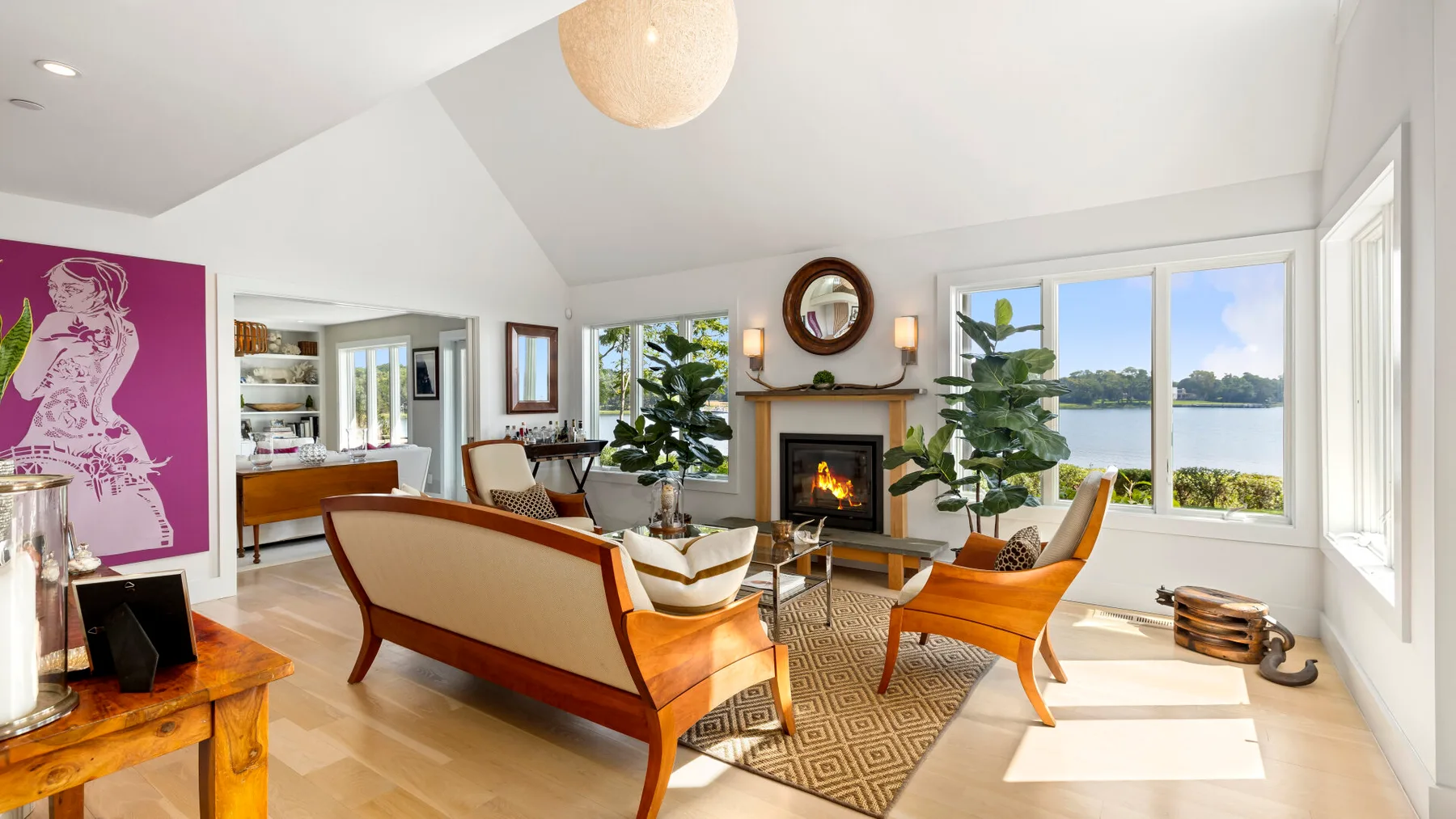 A bright living room with seating, a fireplace, and large windows overlooking the water.