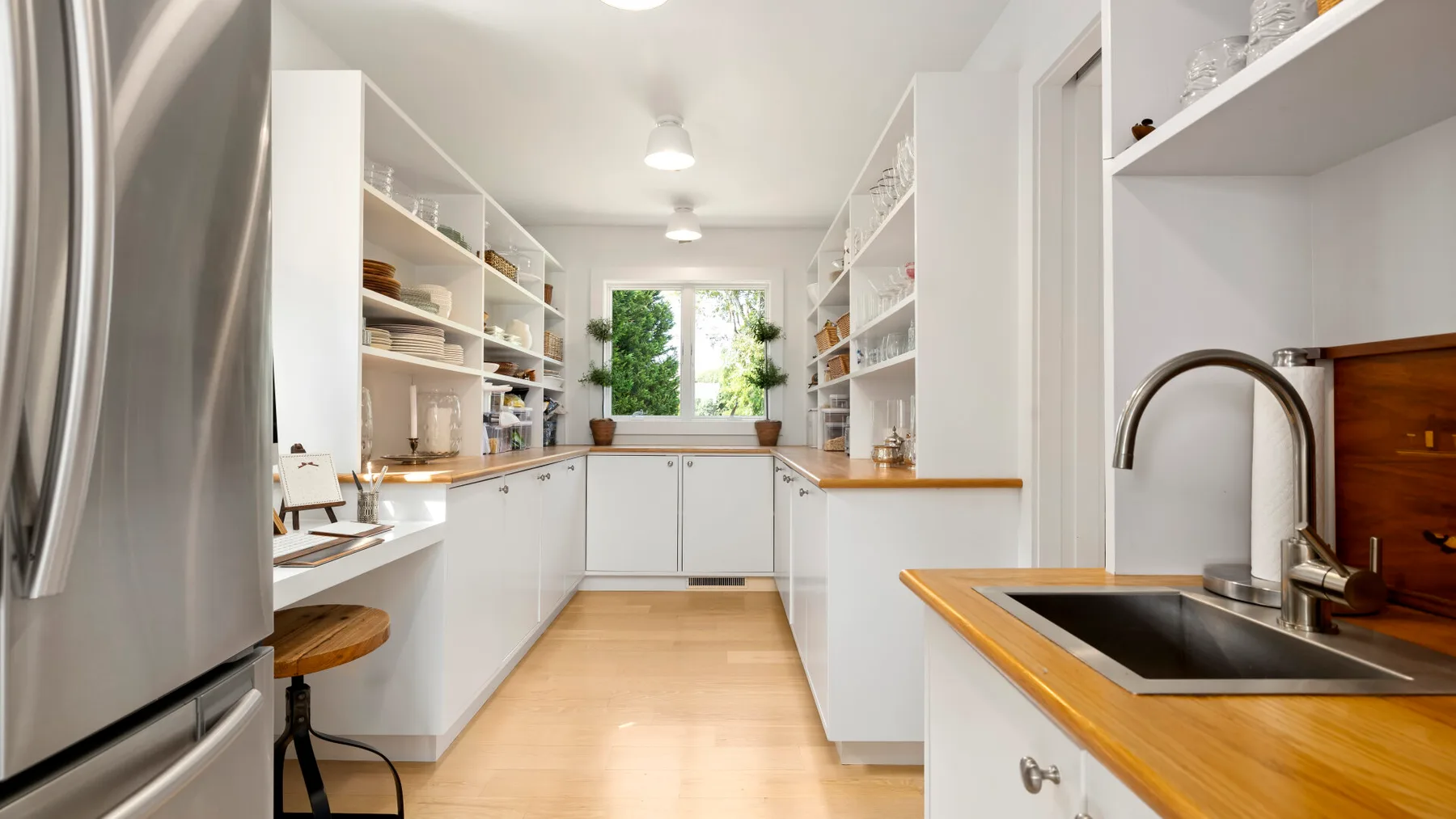 A bright kitchen with white cabinetry, open shelves, and a central work area.