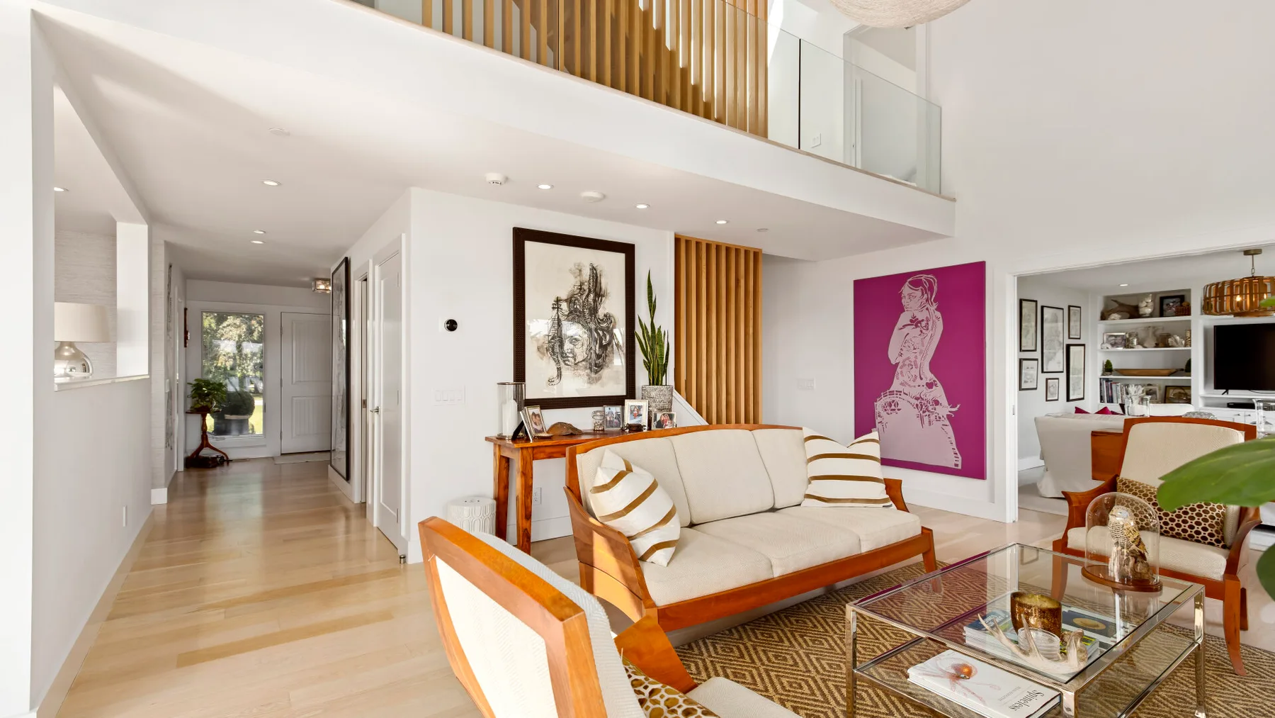 A bright living room with light seating, a glass coffee table, and colorful wall art.