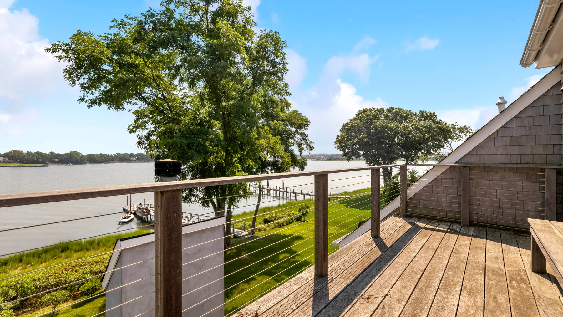 A wooden deck overlooks a grassy shoreline and calm water.