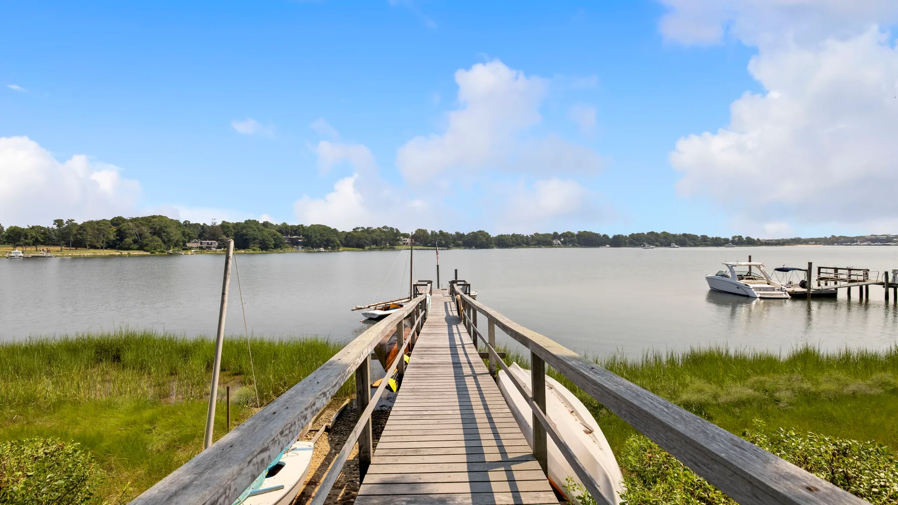 A wooden walkway extends across grassy marshland toward a calm body of water.