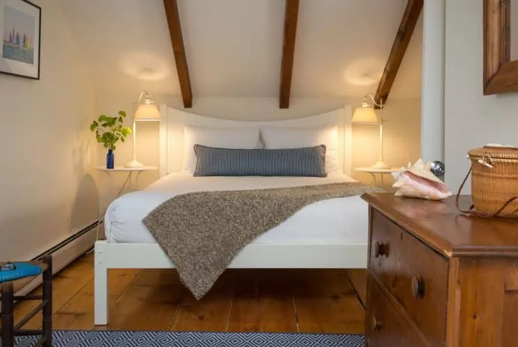 Dormitorio de la Aurora Suite con piso de madera, cabecera y ropa de cama blancas, y cómoda de madera
