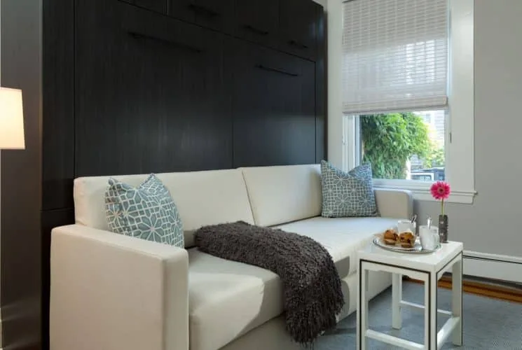 Zona de estar Mary Mitchell con sofá tapizado en blanco y muebles de almacenamiento de madera oscura