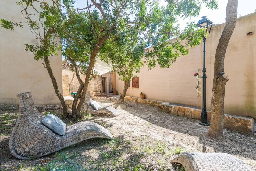 Un patio amurallado con árboles frondosos y tumbonas tejidas.