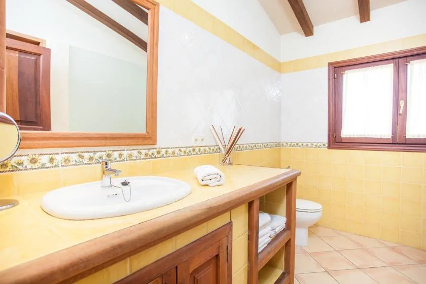Un baño luminoso tiene un lavabo alargado y una ventana.