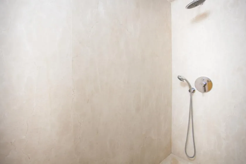 Una ducha con un cabezal de mano instalado en una pared de tono claro.