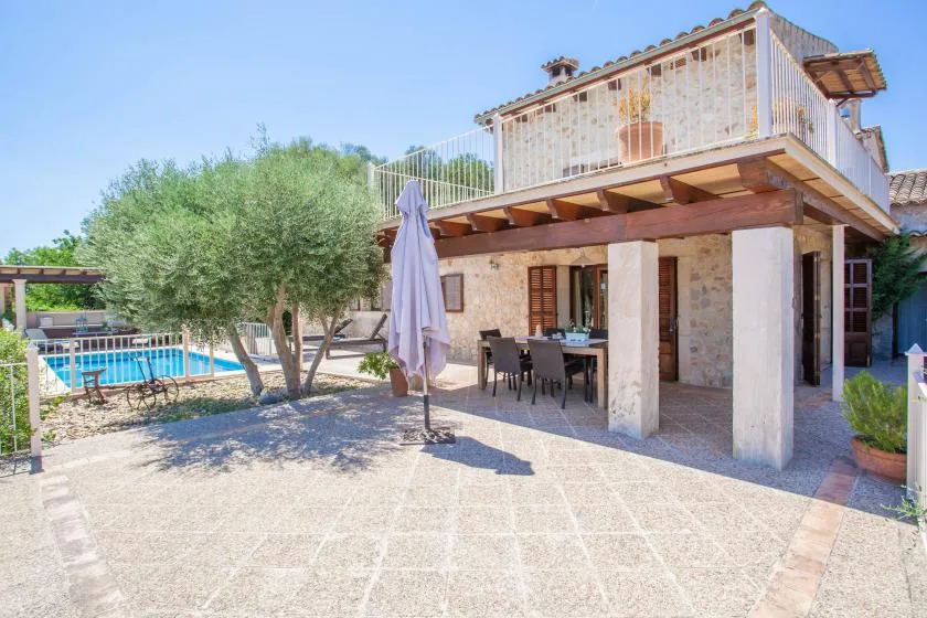 Un patio de piedra con asientos al aire libre está junto a una piscina y un árbol.