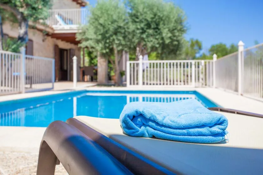 Una piscina junto a un patio, con una toalla azul doblada sobre una tumbona.