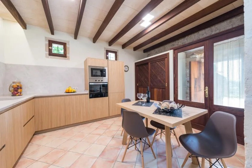 Una cocina y comedor luminosos con gabinetes de madera clara y una mesa.