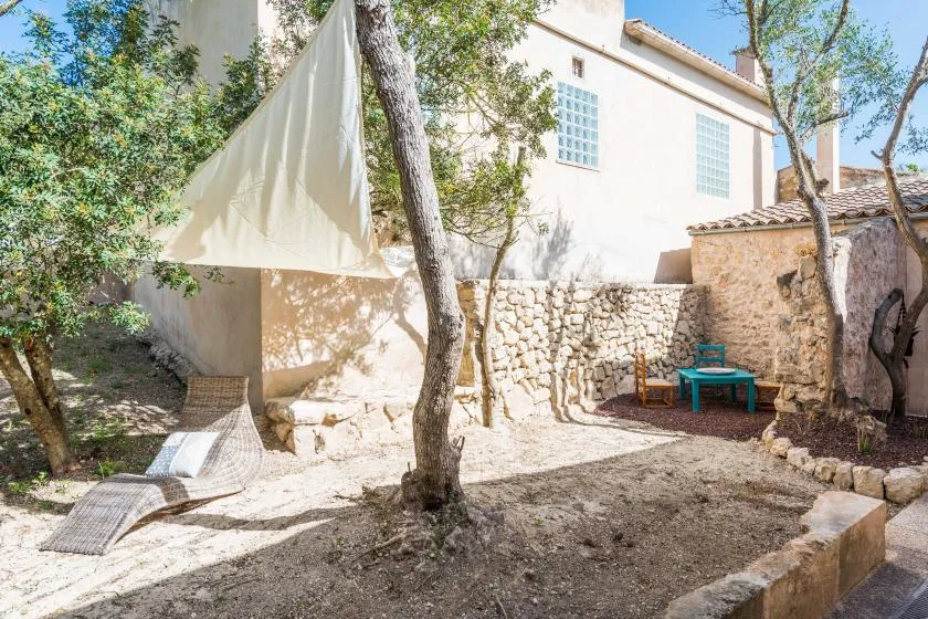 Un patio ajardinado con una zona de estar sombreada junto a un muro de piedra.