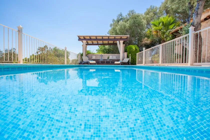 Una piscina rodeada de barandillas, con una zona de asientos a la sombra al fondo.