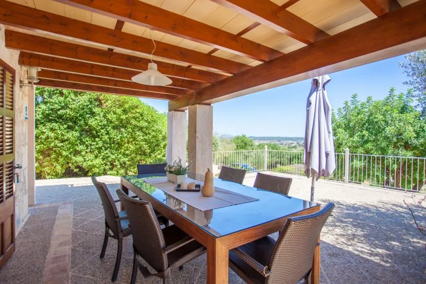 Comedor exterior cubierto con una mesa y vegetación frondosa al otro lado de la barandilla.