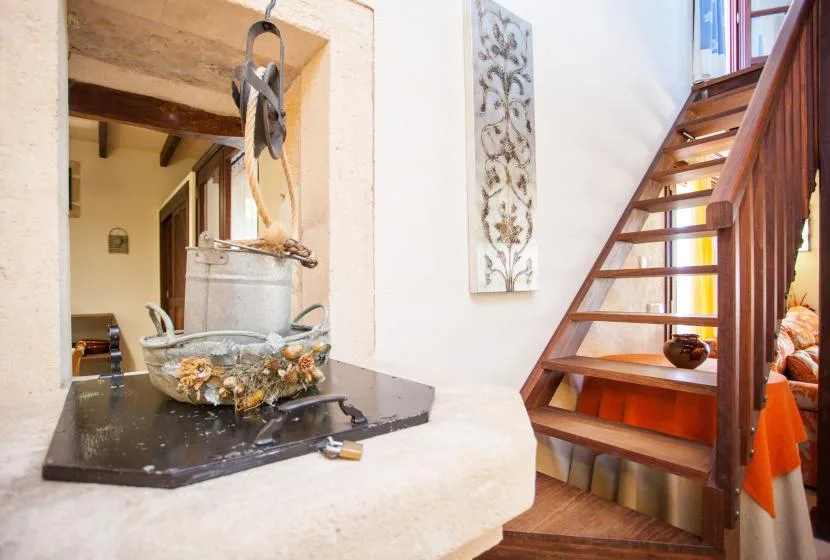 Un hogar rústico de cocina está junto a una escalera de madera en un interior luminoso.