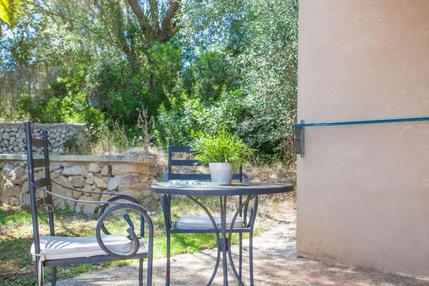 Un patio exterior con una mesa metálica y asientos junto a un jardín.