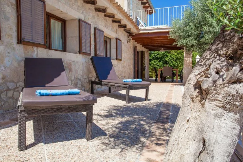 Un patio soleado de piedra con asientos reclinables y una zona de comedor sombreada.